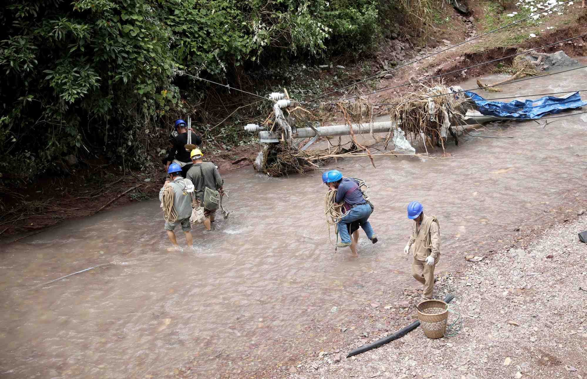 Des electriciens pataugent dans les eaux a proximite d'un poteau electrique endommage par de fortes pluies dans le comte de guzhang