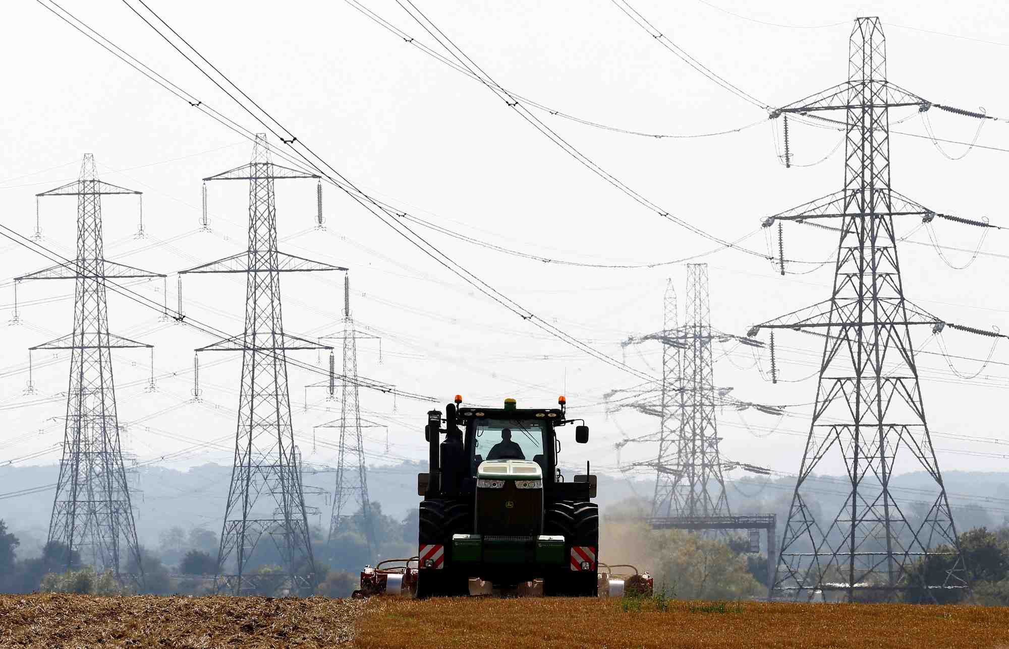 Un agriculteur travaille dans un champ entoure de pylones electriques a ratcliffe-on-soar, en angleterre