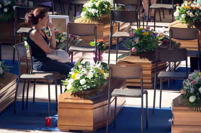 A woman sits next to a coffin to pay her respects as she attends a funeral for the earthquake victims inside a gym in ascoli piceno