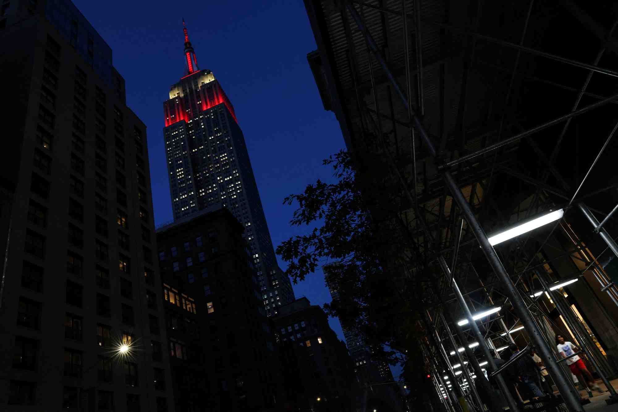 L'empire state building est illumine en rouge alors que des personnes marchent dans le quartier de midtown a new york