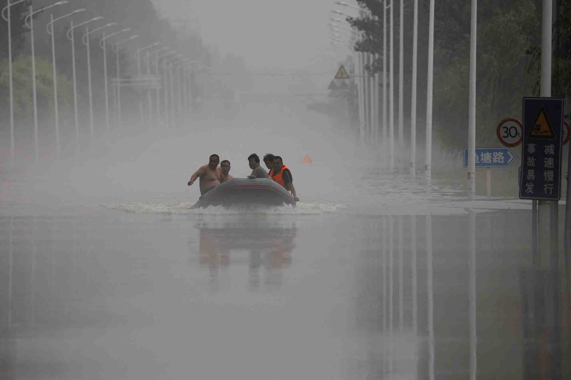 Des gens traversent en bateau une route inondee apres les pluies du typhon doksuri, a zhuozhou en chine