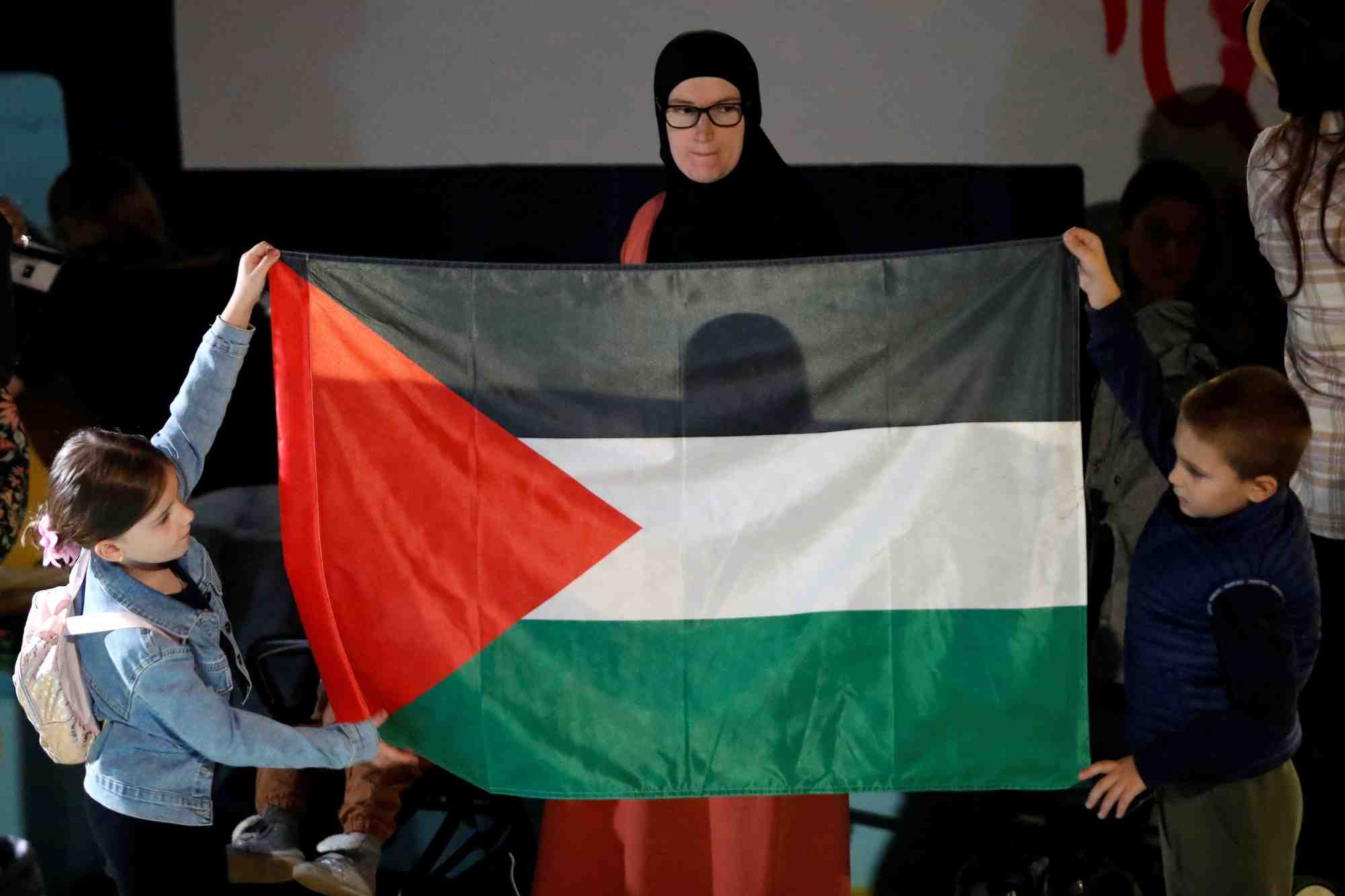 Une femme regarde des enfants tenant un drapeau palestinien