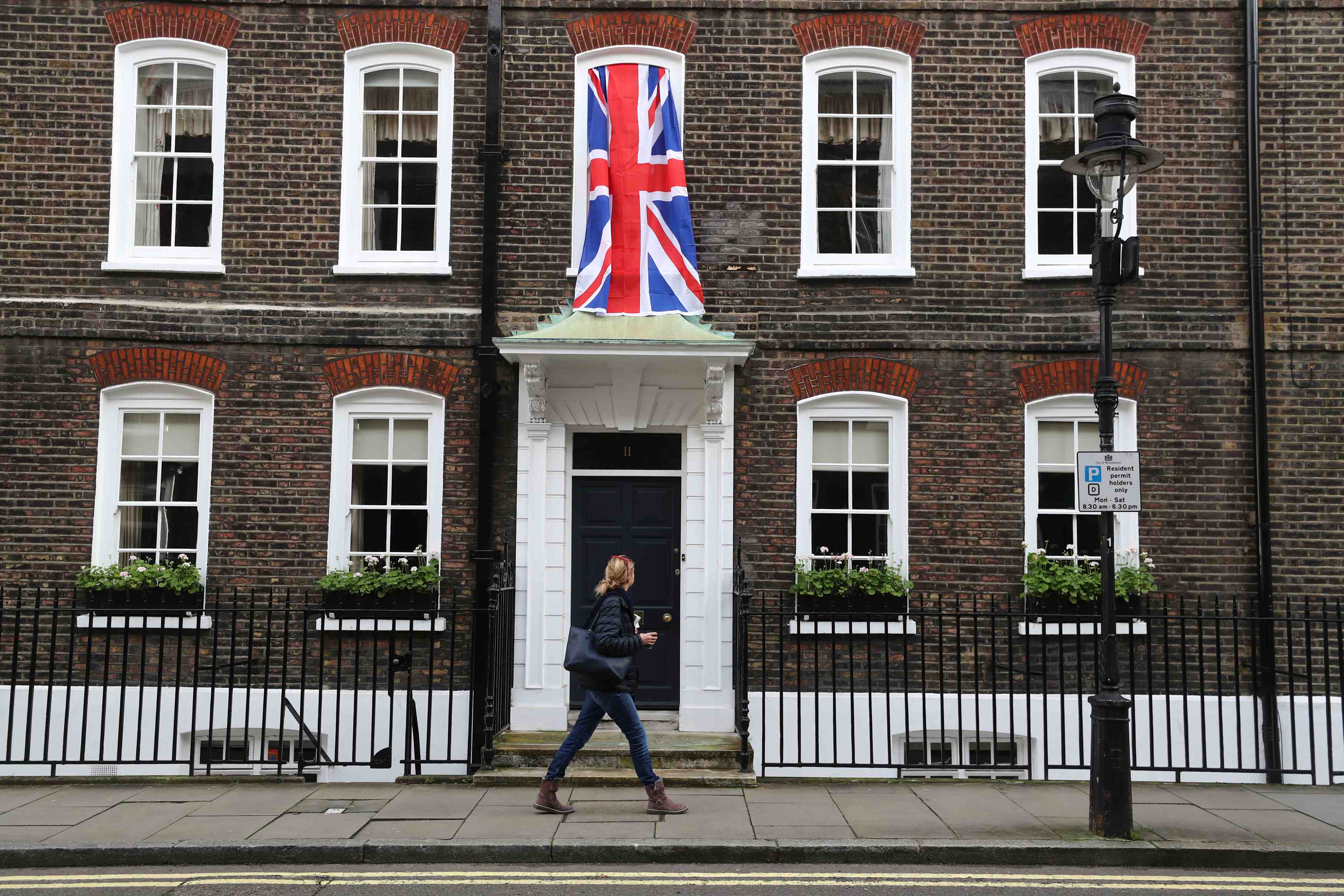 Woman walks past a union jack flag hanging on a house in westminster in london