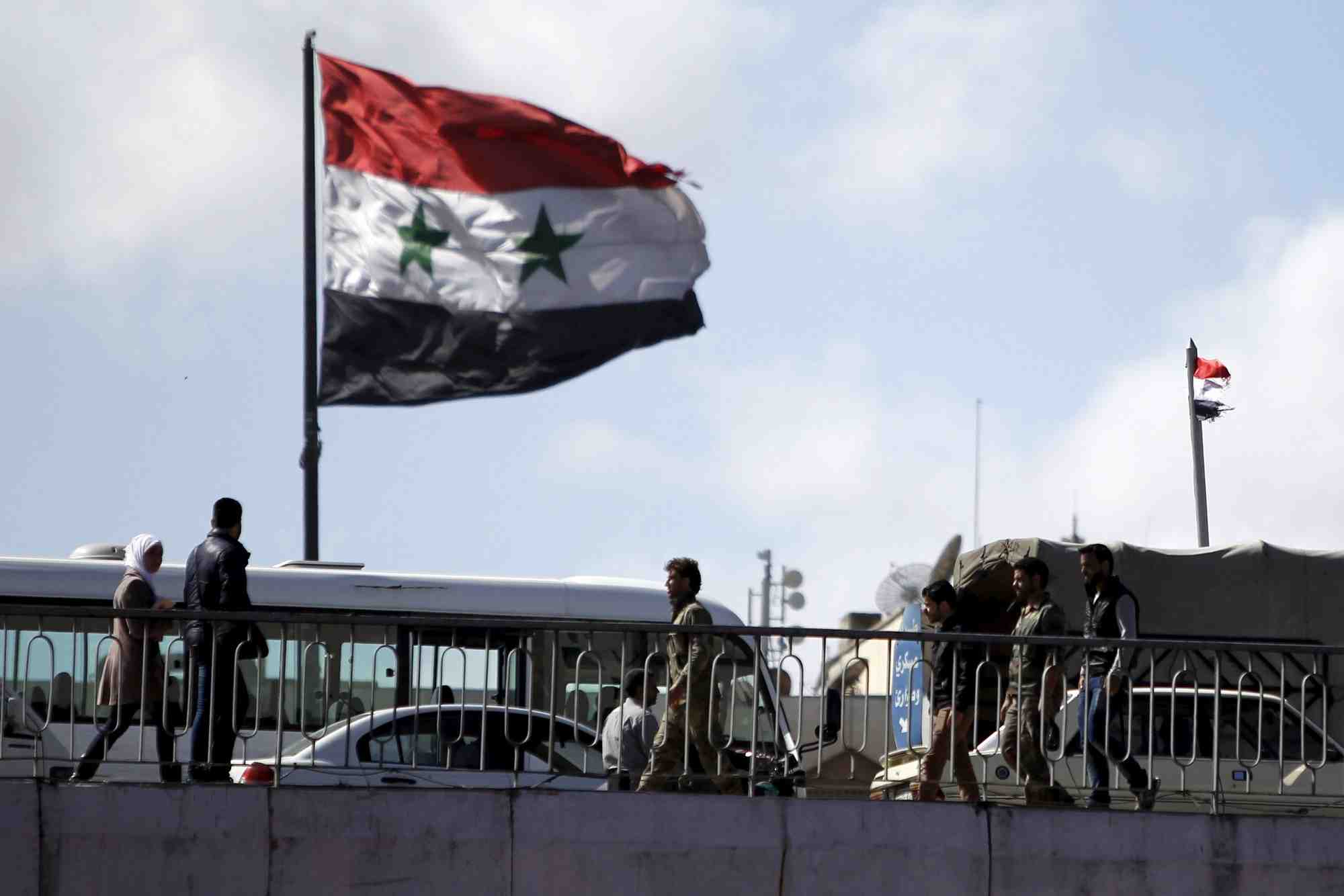 Des personnes marchent pres d'un drapeau syrien sur le pont du president a damas