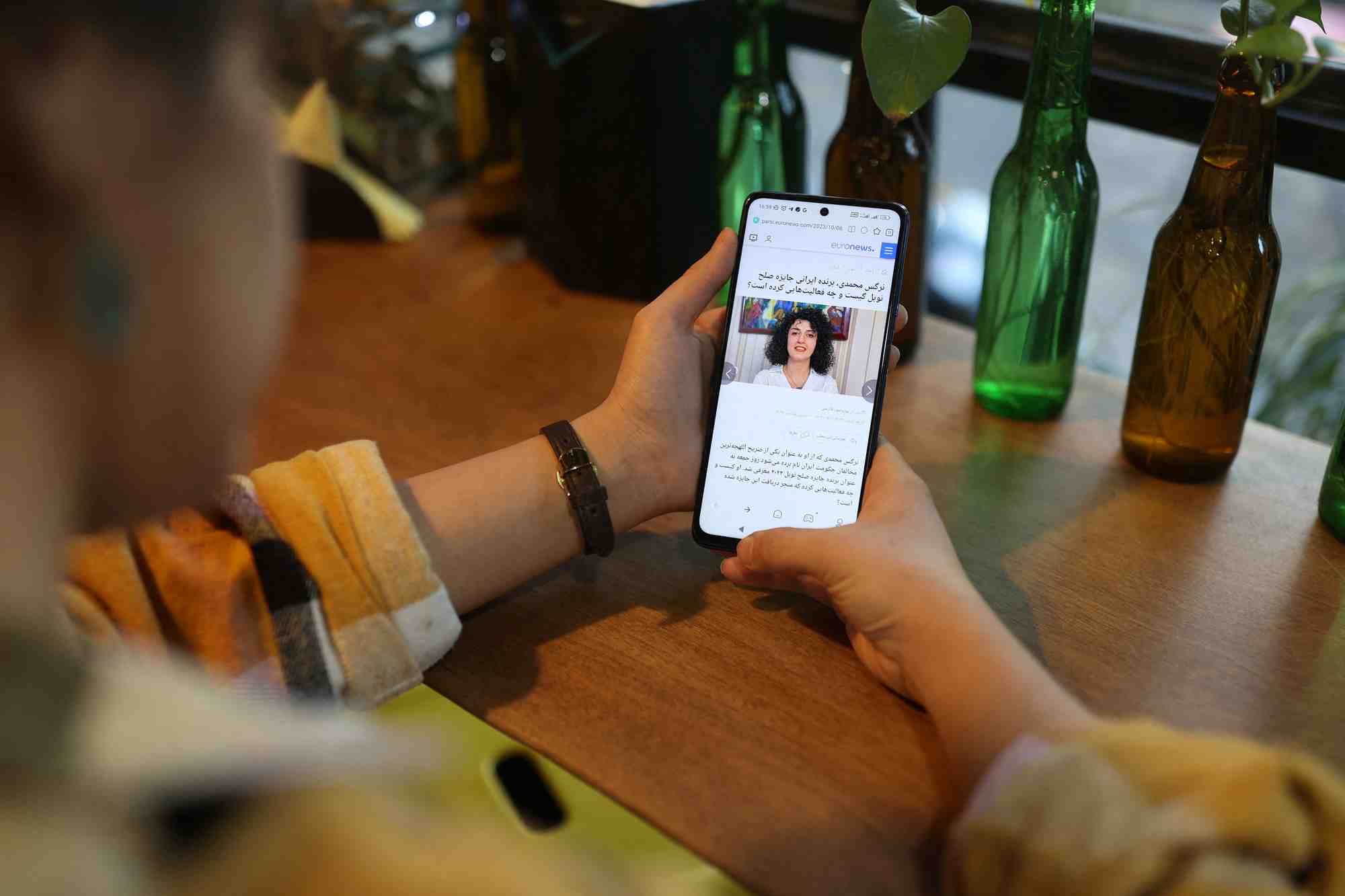 Une femme iranienne regarde sur son telephone portable la nouvelle que la militante iranienne des droits de l'homme narges mohammadi a gagne le prix nobel de la paix, dans un cafe a teheran