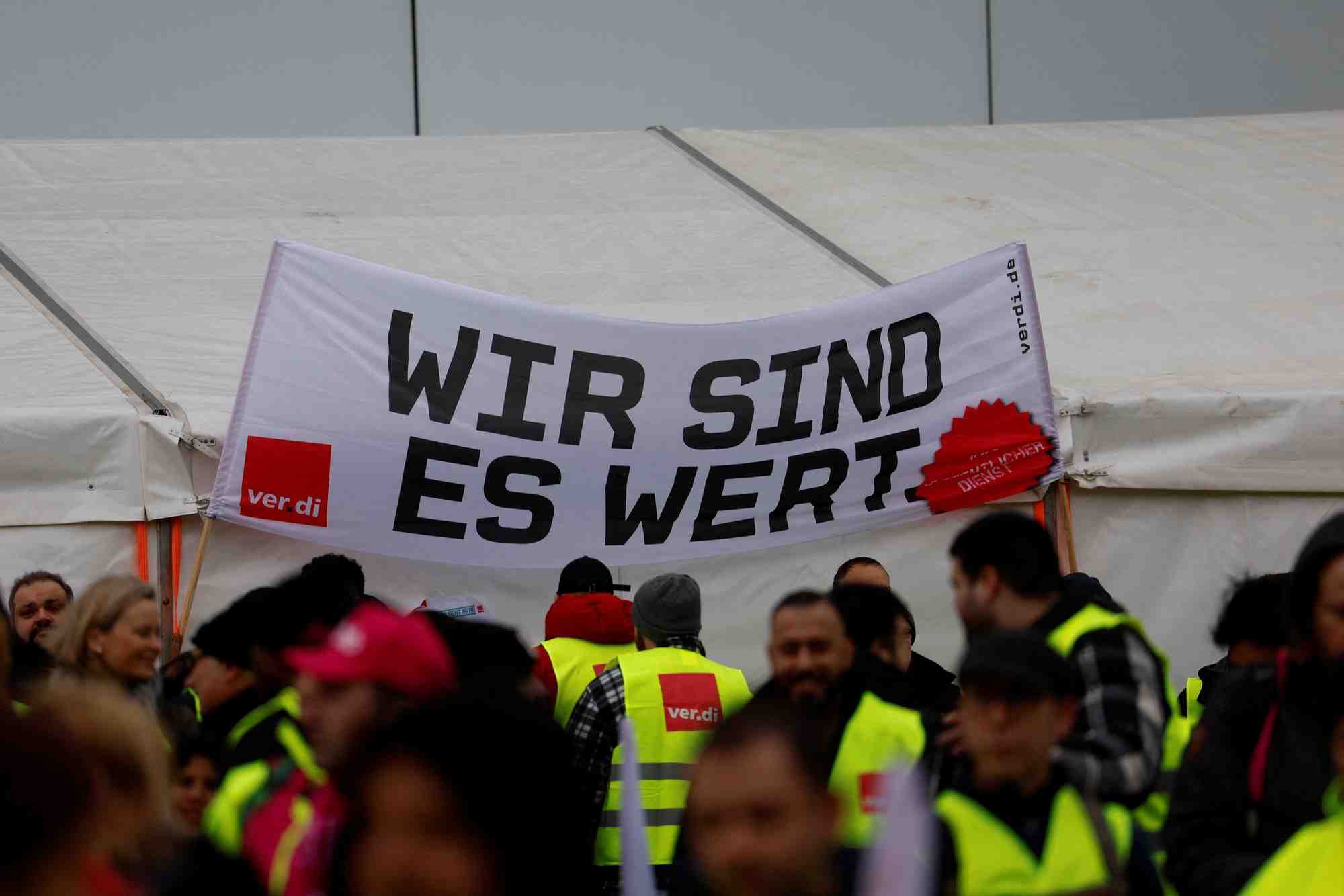Photo des employes qui tiennent une banderole "nous en valons la peine" lors d'une greve aux aeroports de francfort, munich, stuttgart, hambourg, dortmund, hanovre et breme