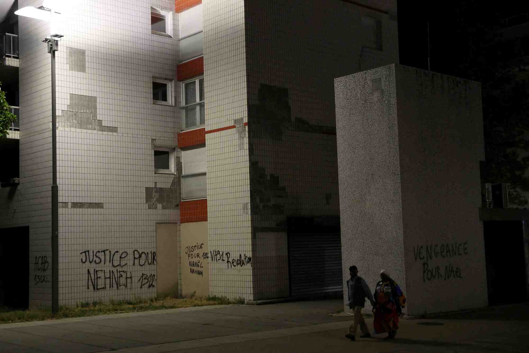 Des habitants passent devant des phrases ecrites sur les murs des immeubles de nanterre, le quartier du jeune de 17 ans tue par un policier lors d'un controle routier