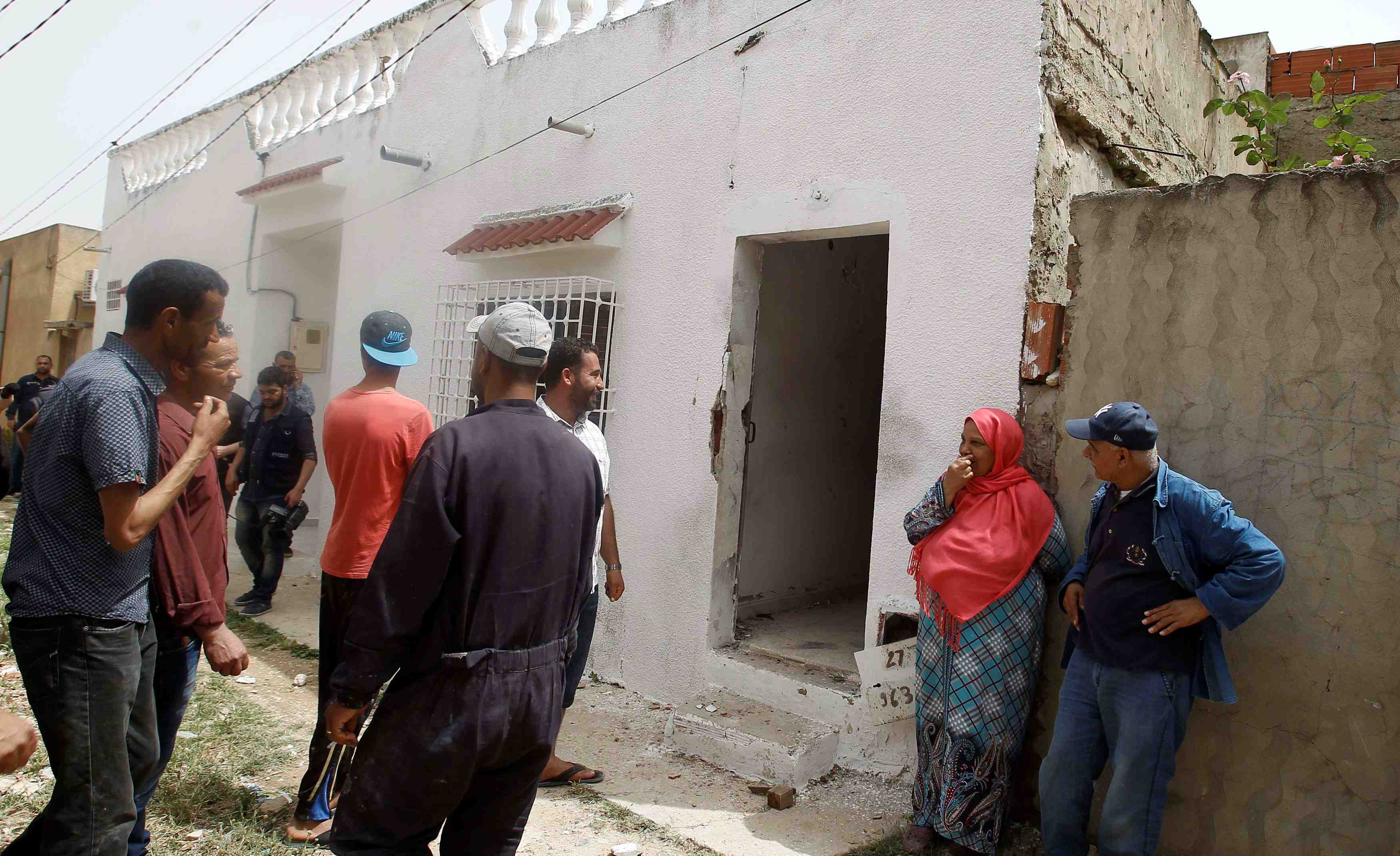 People stand near a house which was damaged during a security operation that saw a clash between tunisian security forces and suspected militants in tunis