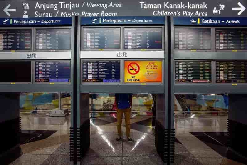 A man stand near flight information boards at kuala lumpur international airport