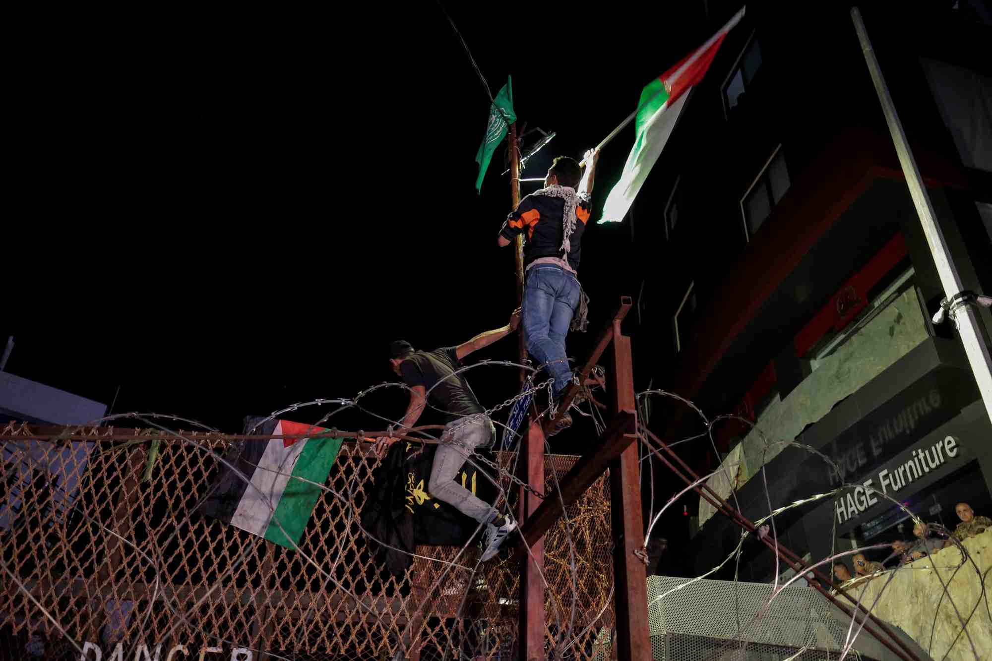 Les manifestants libanais brandissent des drapeaux palestiniens tout en escaladant la cloture de l'ambassade americaine a beyrouth, au liban