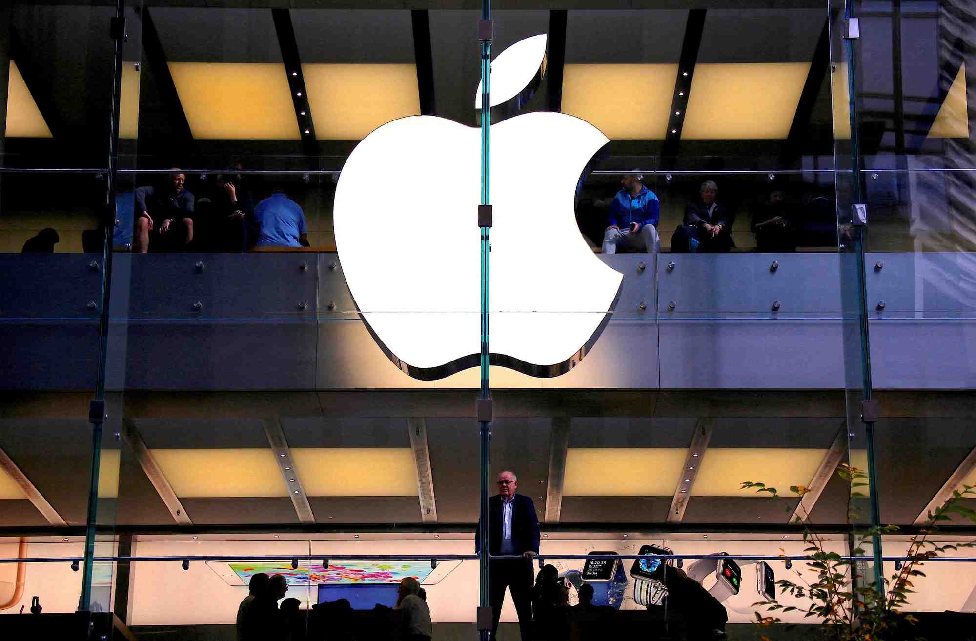 Un client se tient sous un logo apple illumine alors qu'il regarde par la fenetre du magasin apple situe dans le centre de sydney
