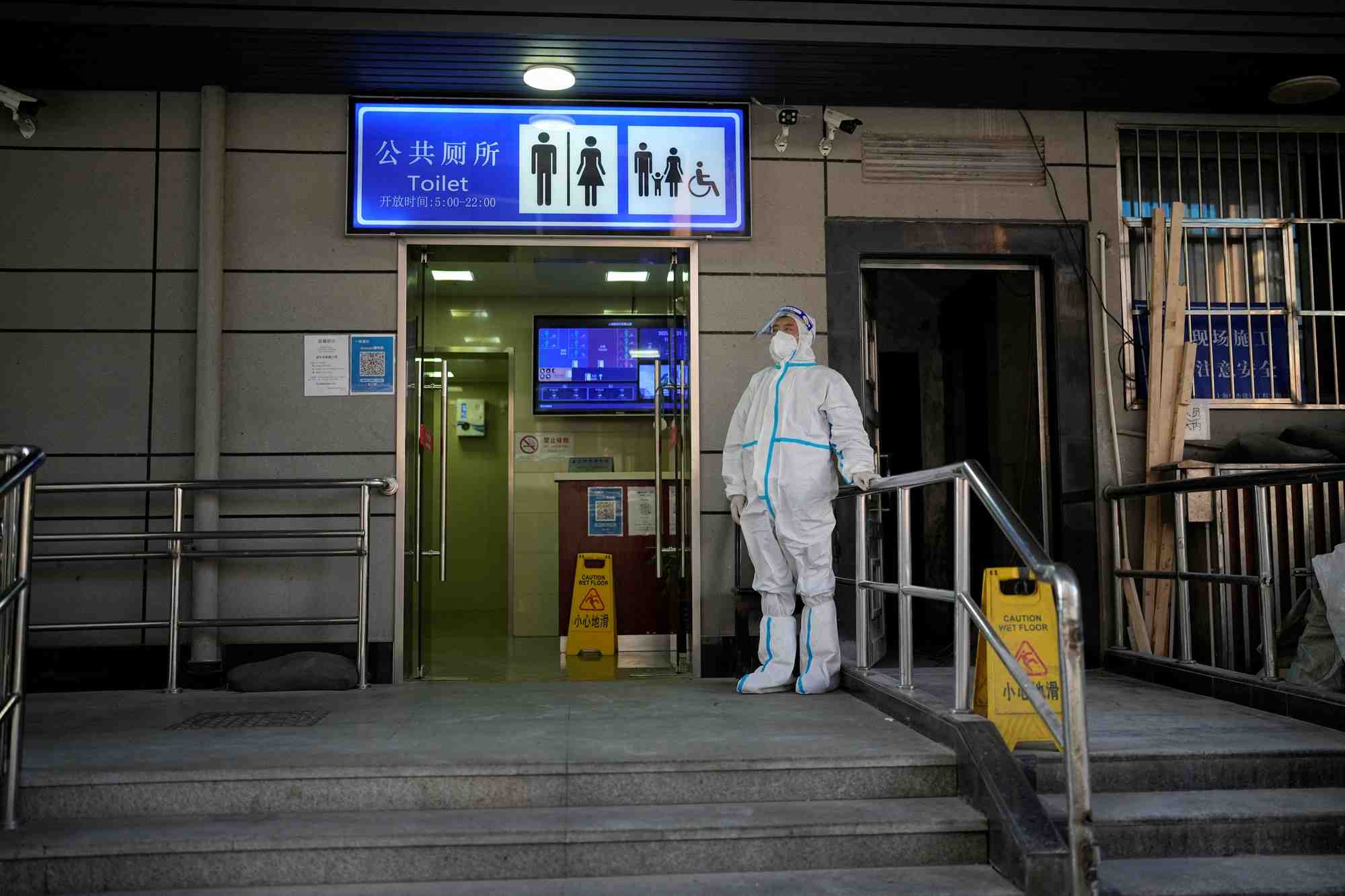 Un travailleur en combinaison de protection surveille l'exterieur d'une toilette publique a shanghai