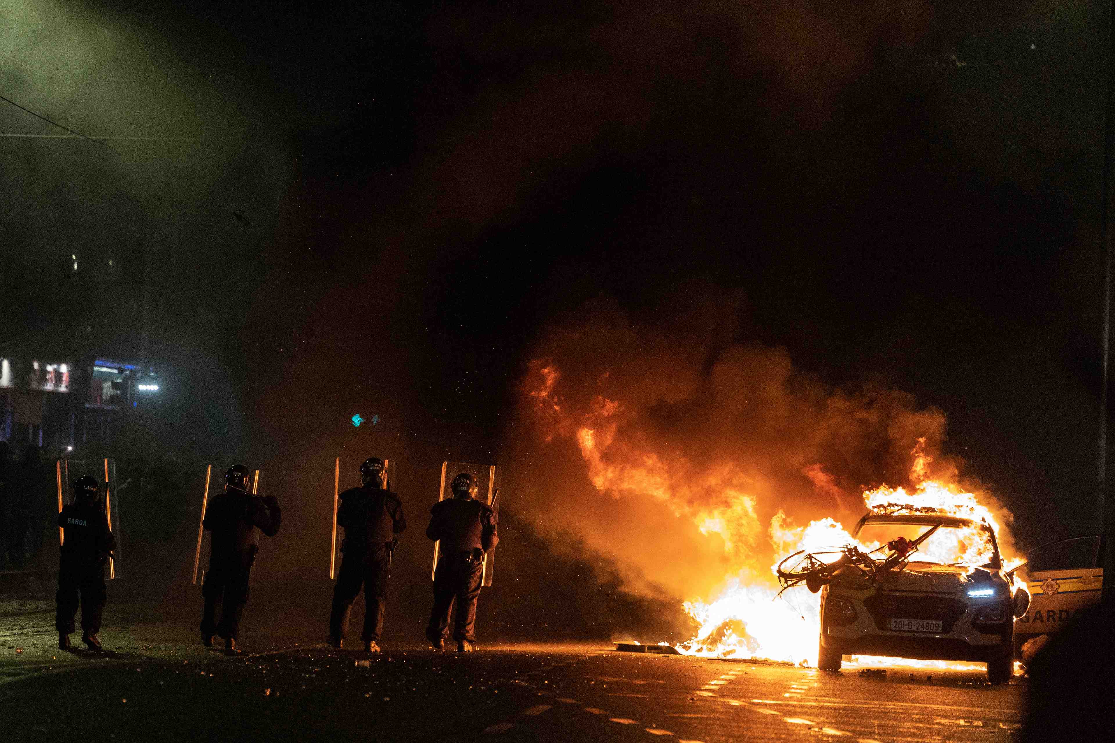 Des policiers font face a des manifestants a cote d'une voiture de police en feu, a la suite d'une attaque au couteau survenue plus tot dans la capitale irlandaise