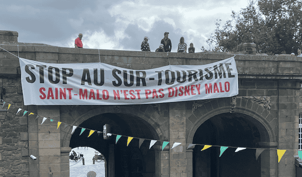 Dimanche 16 juillet au matin, une large banderole a été déroulée en haut des remparts de la vieille ville de Saint-Malo (Ille-et-Vilaine) pour dénoncer le surtourisme. (@SoLeNoenLess)
