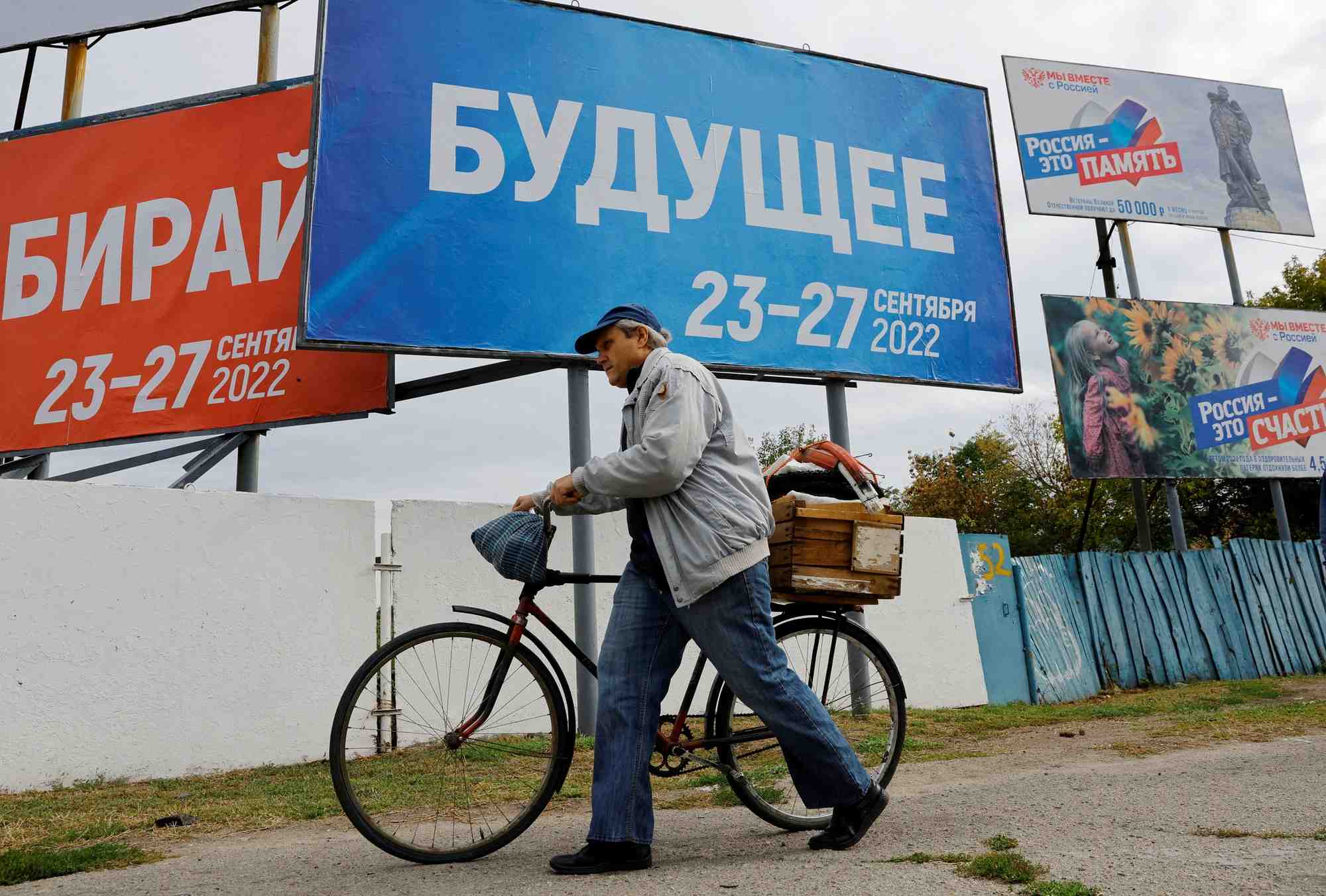 Un homme avec un velo devant des panneaux au sujet d'un referendum sur le rattachement a la russie des regions d'ukraine controlees par la russie