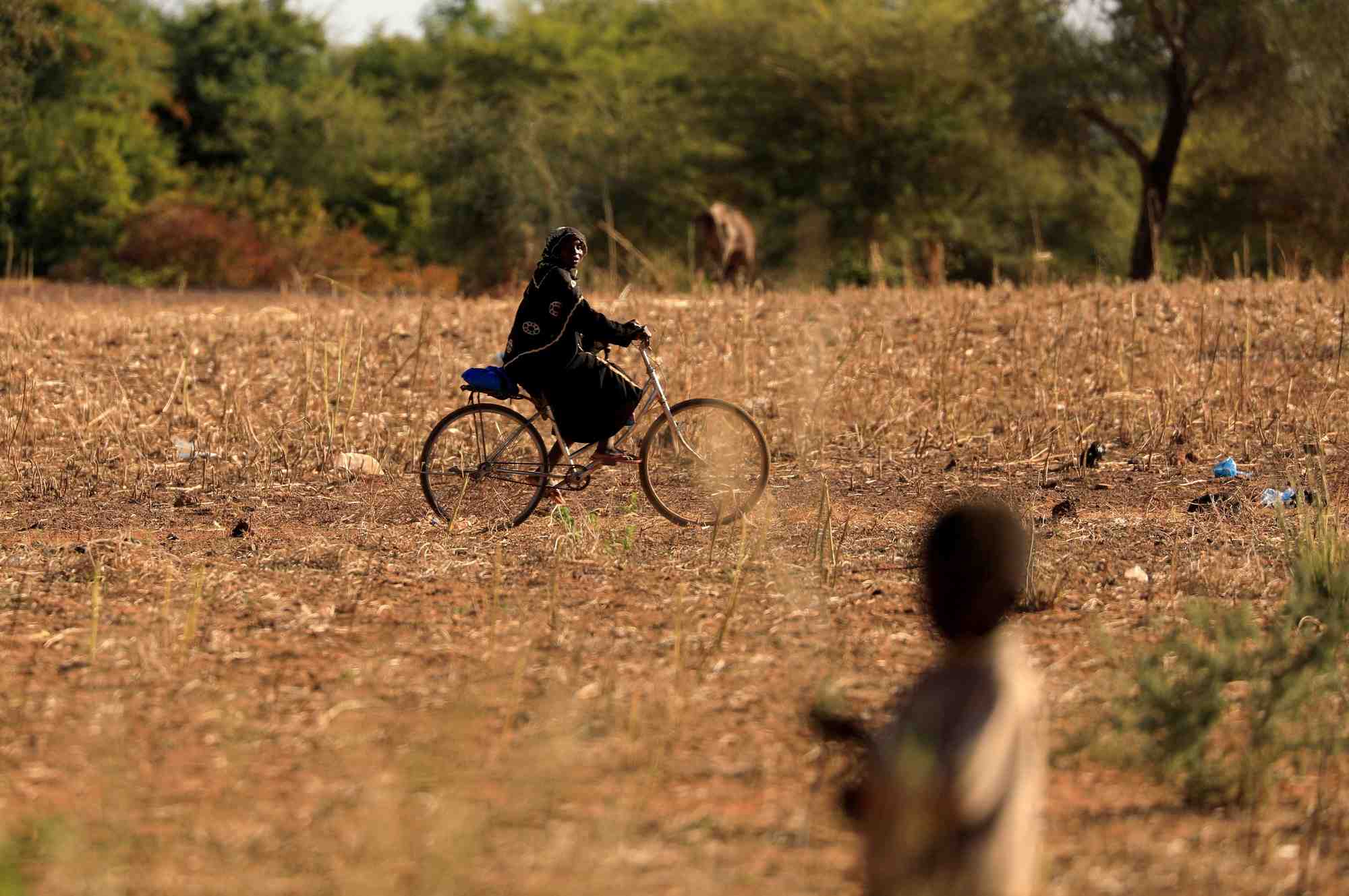 Photo d'archives: un enfant qui a fui avec ses parents les attaques de militants armes dans la region du sahel observe une femme a velo dans un camp de personnes deplacees au burkina faso