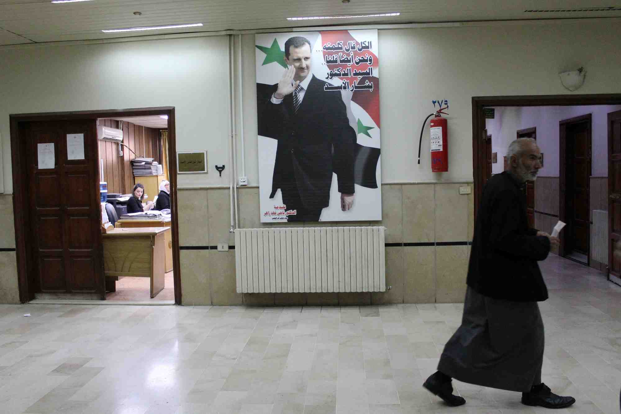 Un homme passe devant une photo du president syrien bashar al-assad a l'interieur de l'hopital ibn al-nafis a damas