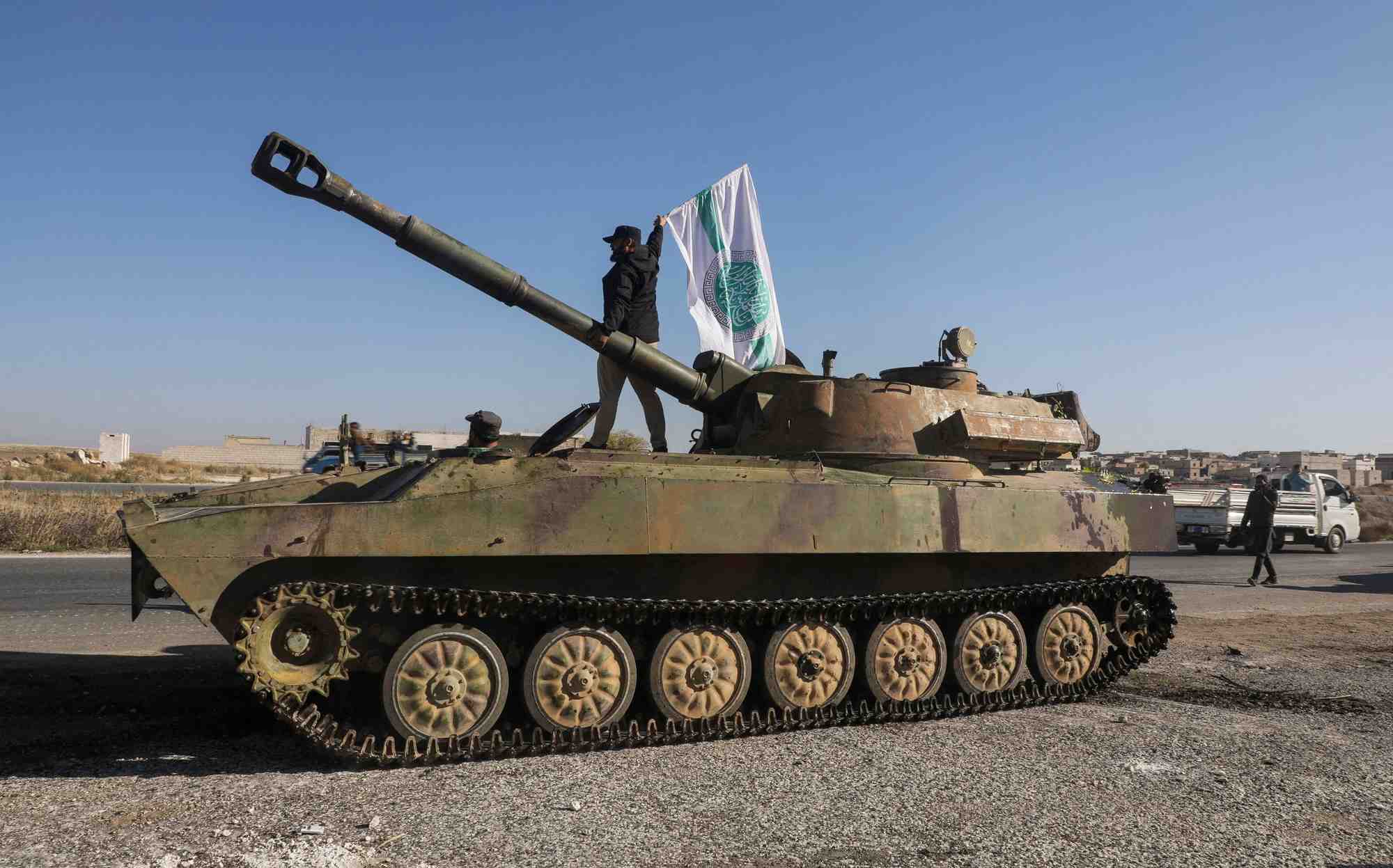 Un combattant rebelle se tient au-dessus d'un vehicule militaire et porte le drapeau de hayat tahrir al-sham a saraqeb
