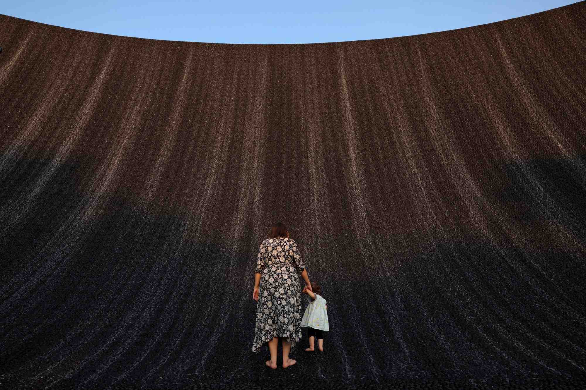 Une femme tient la main d'un bebe alors qu'ils profitent tous deux de la cascade de l'expo a la cop28, a dubai