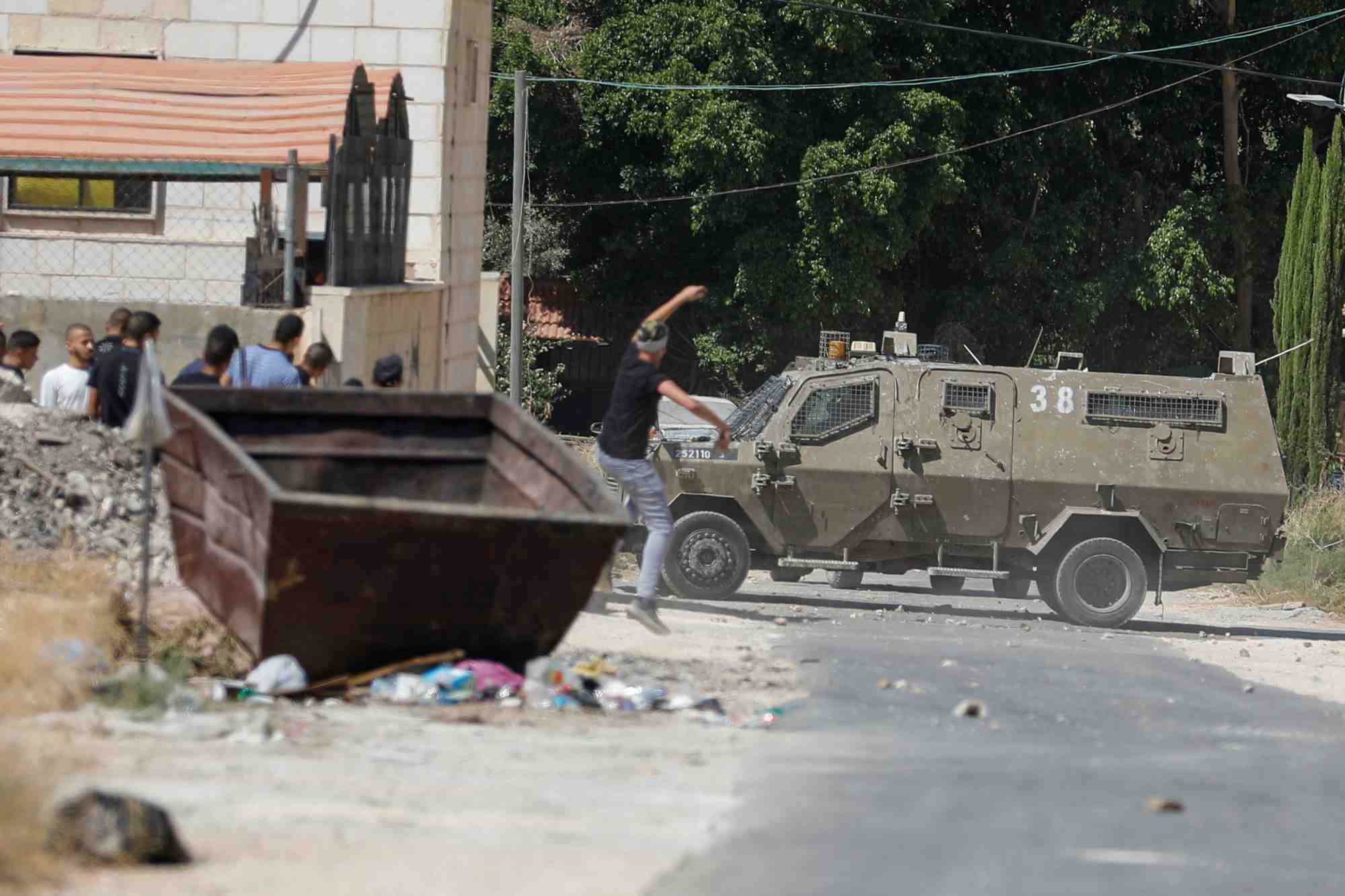 Un palestinien lance une pierre sur un vehicule de l'armee israelienne