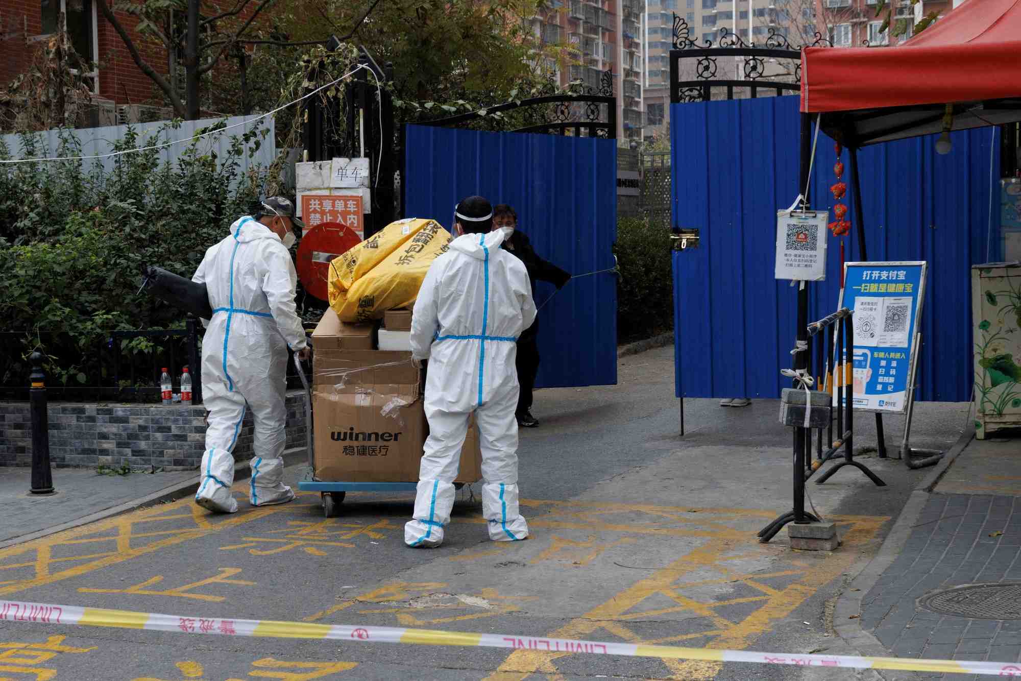 Des hommes portant des combinaisons de protection livrent des colis dans un complexe residentiel qui a ete place en quarantaine a pekin