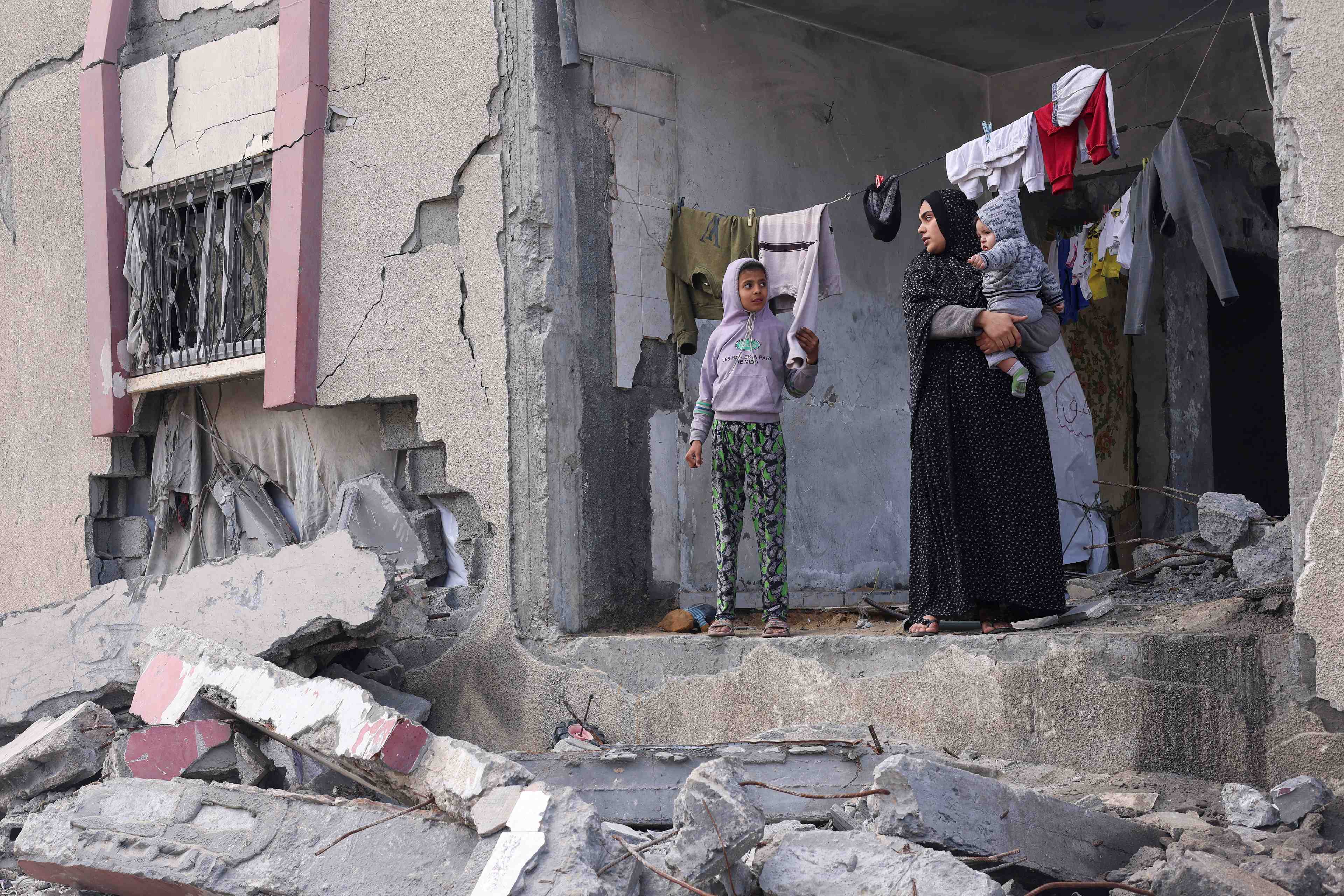 Une palestinienne tient son enfant dans les bras alors qu'elle se tient devant une maison endommagee par les frappes israeliennes, a rafah