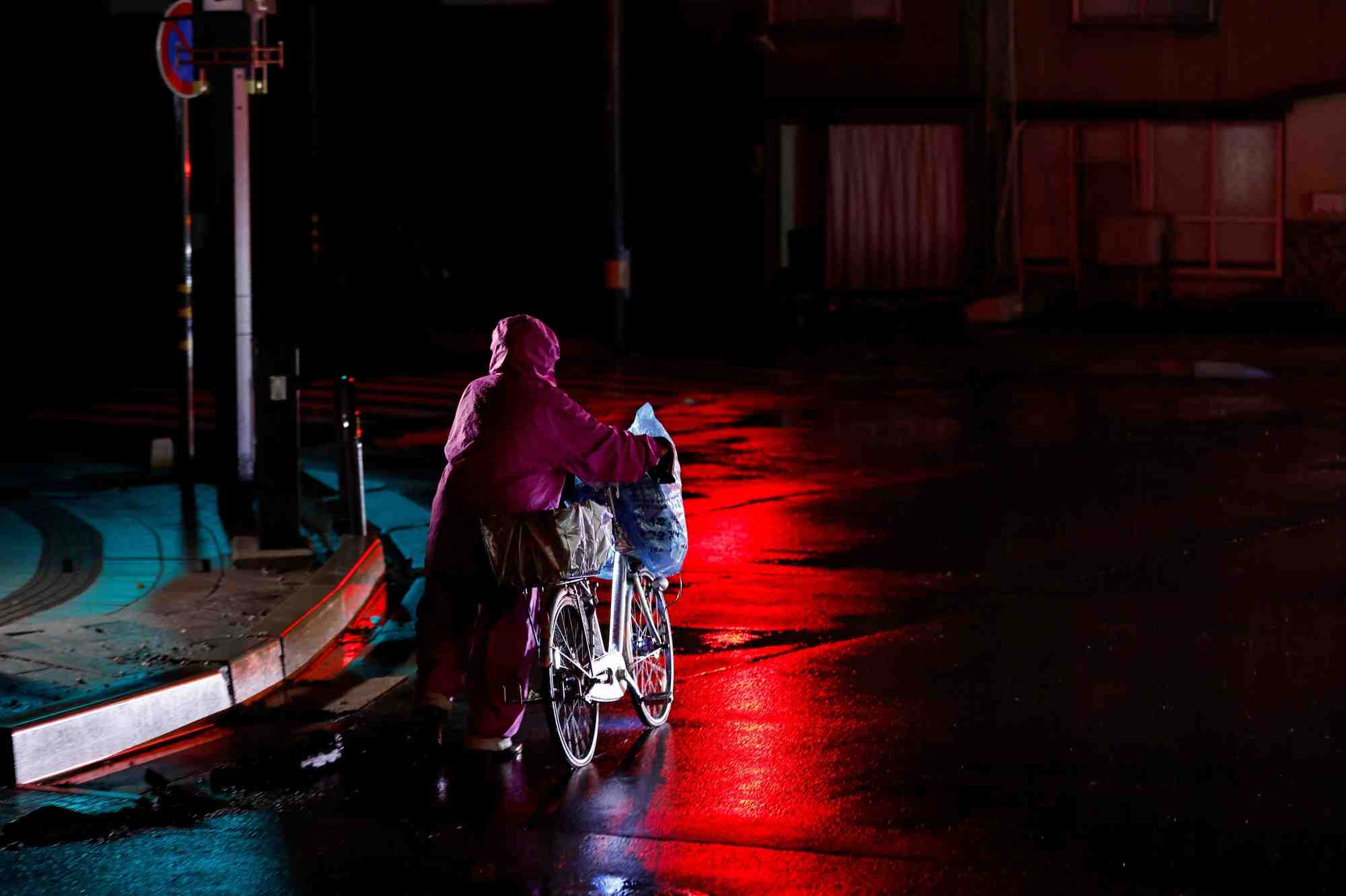Photo d'une personne qui transporte des affaires et pousse un velo, a la suite d'un tremblement de terre a wajima, au japon