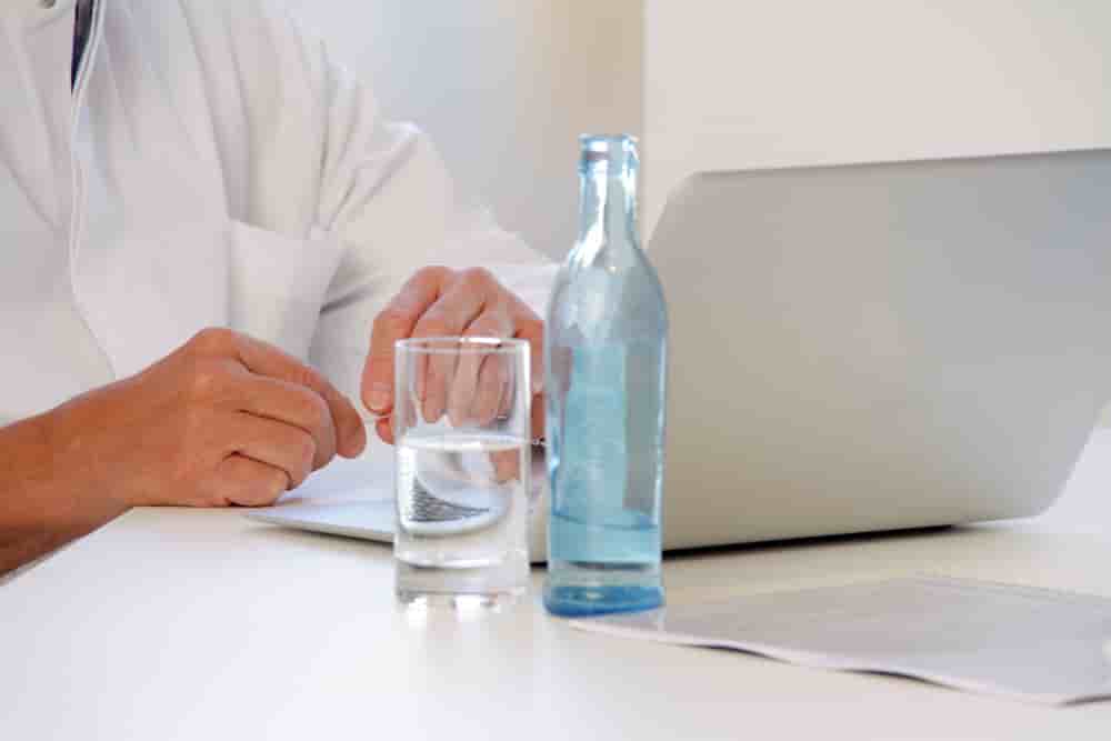 Arzt mit Mineralwasser auf dem Schreibtisch