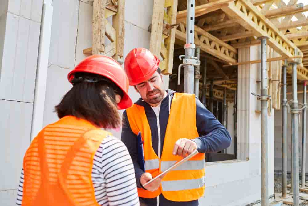 Polier und Architektin mit Tablet Computer vor dem Rohbau einer Baustelle für den Hausbau - Polier und Architektin mit Computer vor dem Rohbau