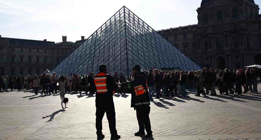 Des visiteurs font la queue devant la pyramide du Louvre.