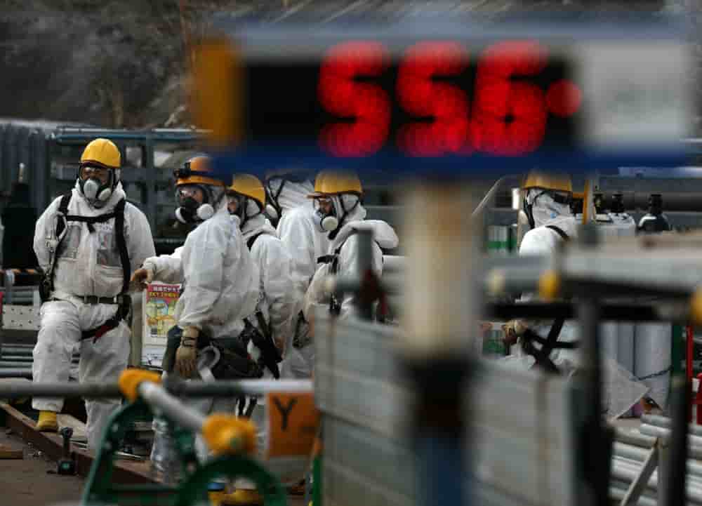 Des travailleurs vêtus de combinaisons de protection et de masques mènent une opération de démantèlement à proximité des bâtiments des réacteurs n°2 et n°3.