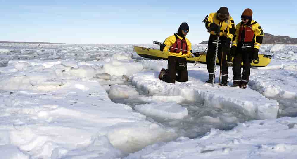 À côté de son canot à glace, l'équipe mesure la température de la glace et de l'eau.