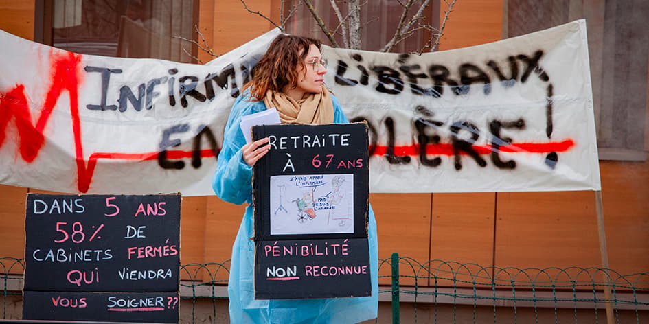 Une infirmiere liberale tient un panneau sur lequel est indique Retraite a 67 ans, penibilite non reconnue, avec un dessin humoristique au milieu. Gap, Hautes-Alpes, 12 février 2024.