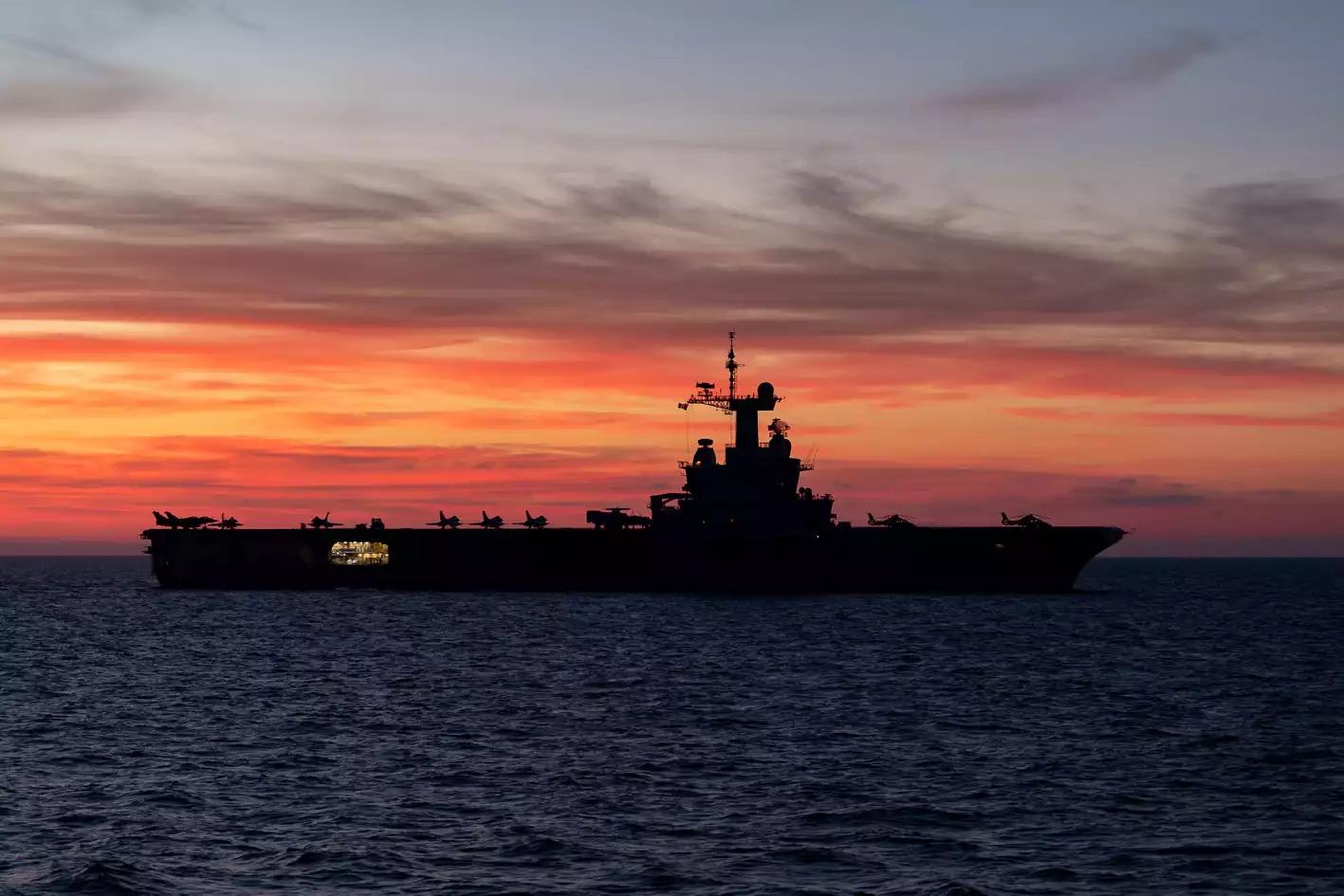 Porte-avions Charles de Gaulle devant un coucher de soleil.