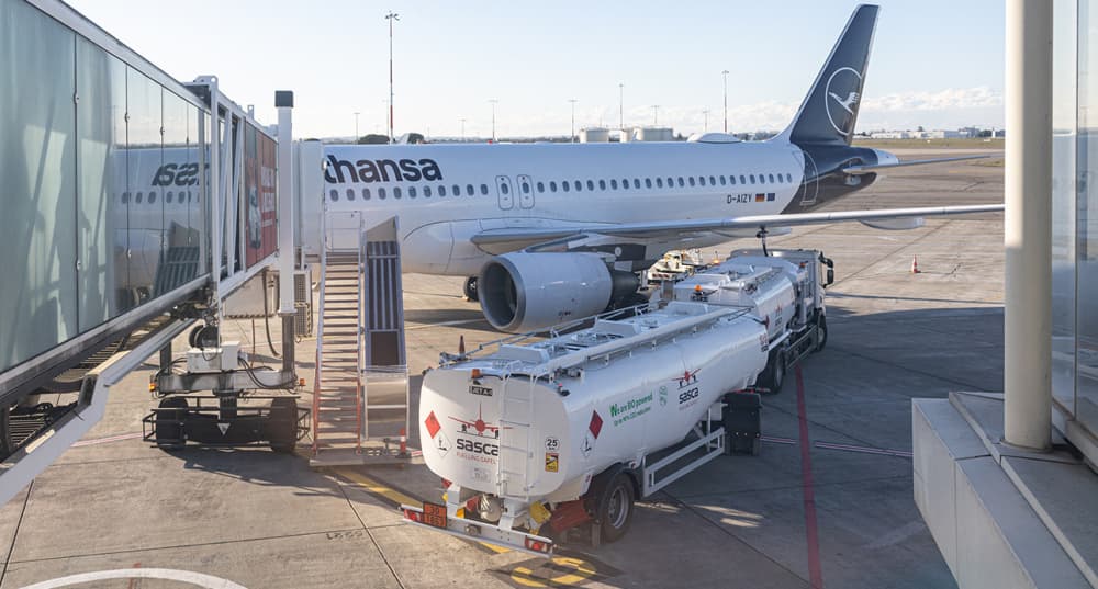 Un avion de la compagnie Lufthansa est stationné à une porte tandis qu'un camion-citerne SASCA le dessert sur le tarmac de l'aéroport de Toulouse Blagnac.