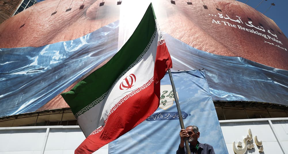 Un homme tient un drapeau iranien à proximité d’un stand anti-américain. Panneau d'affichage représentant le président américain Donald Trump et le détroit d'Ormuz, à Téhéran, Iran, le 30 mai 2026.